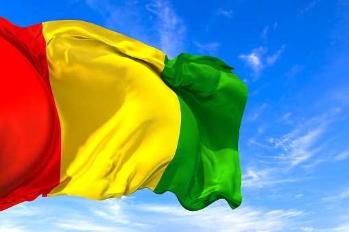 The national flag of Guinea with fabric texture waving in the wind on a blue sky. 3D Illustration