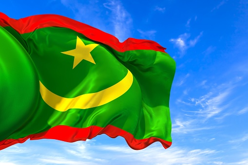 The national flag of Mauritania with fabric texture waving in the wind on a blue sky. 3D Illustration