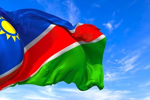 The national flag of Namibia with fabric texture waving in the wind on a blue sky. 3D Illustration
