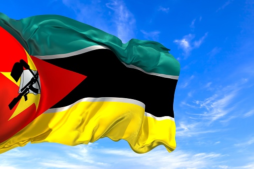 The national flag of Mozambique with fabric texture waving in the wind on a blue sky. 3D Illustration