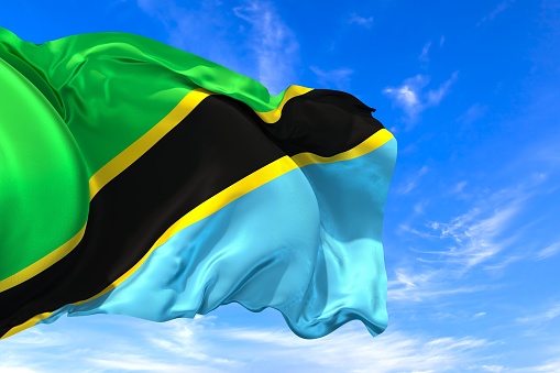 The national flag of Tanzania with fabric texture waving in the wind on a blue sky. 3D Illustration