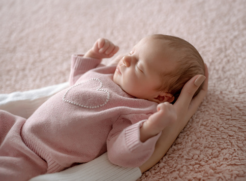 Baby Girl In Pink Outfit Sleeps While Mom Holds Her During Newborn Photo Session In Studio