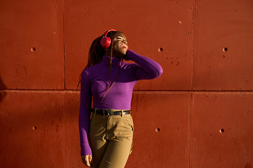 Joyful woman in purple top with headphones against an orange wall.
