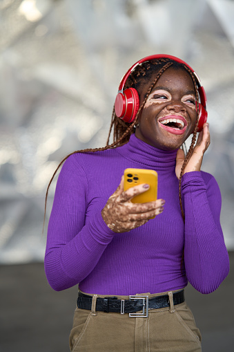 Gleeful woman with vitiligo, engaged with music on red headphones, using her smartphone
