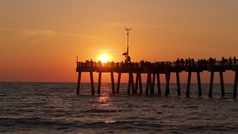 Venice, Florida. Many fishermen tourists enjoying vacation time at sunset on fishing pier. Seaside summer activities