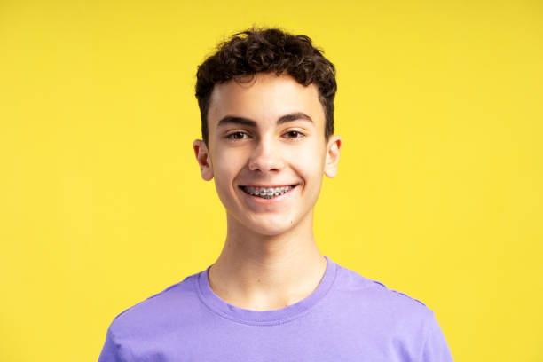 istock Smiling confident boy with dental braces on teeth looking at camera isolated on yellow background 1938263098