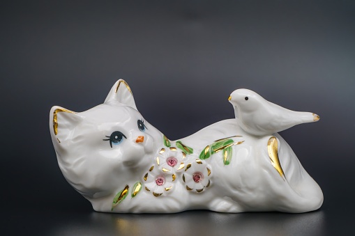 Porcelain playful cat, ceramic statuette. Dove, embellishment, petals and leaves gilded edges. Hand-painted refined. Shiny surface, collectible item. Graceful posture, handcrafted. Black background