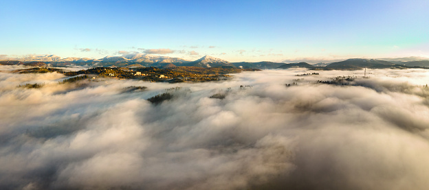 Aerial view of a small village houses on hill top in fall foggy mountains at sunrise.