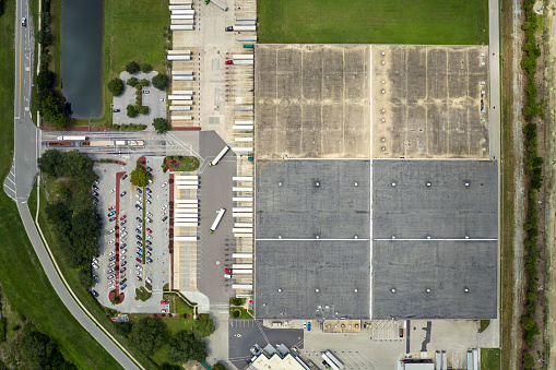 Top view of giant logistics center with many commercial trailer trucks unloading and uploading retail products for further shipment. Global economy concept.