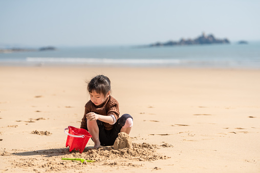 A Chinese little girl playing with sand on the beach