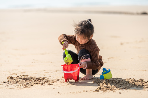 An Asian little girl is playing with sand with toys on the beach