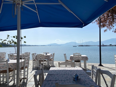 View of the sea from an empty waterfront seafood restaurant with a large blue umbrella in the town of Nea Artaki on the island of Euboea (Evia), Greece in the fall