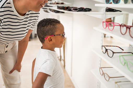 A mixed race woman and boy try on fashionable glasses, showcasing their shared interest in trendy optical wear in a retail setting.