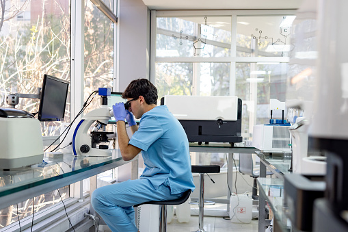 Latin American scientist doing research at the laboratory looking at microorganisms using a microscope - science concepts