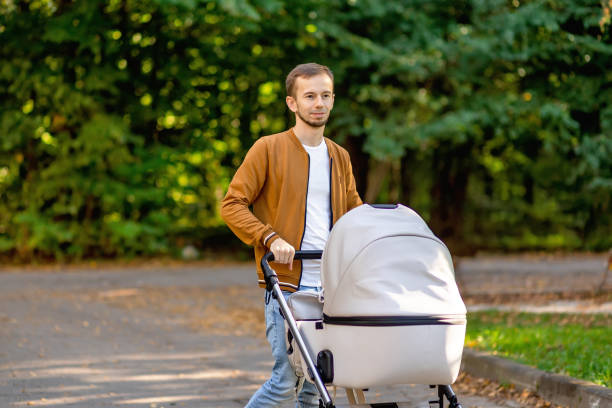 Man with baby stroller walks in the summer park at daylight