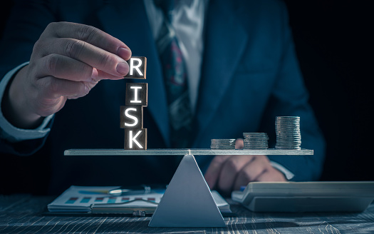 Economic risk management concept. Businessman holding wooden block with word RISK. With level coin balance, banking, financial crisis, bad debt, inflation and interest rates. Investment protection.