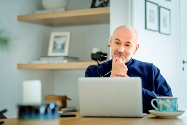 istock Mid aged man wearing casual clothes and using laptop for work while sitting at home 1938690073