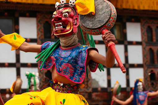 Bumthang Valley, Bhutan - April 17, 2008: Masked monk wearing a traditional elaborate brocaded costume with a vivid yellow skirt and a deer mask with antlers performs religious rituals during the annual tsechu festival in Domkhar village.