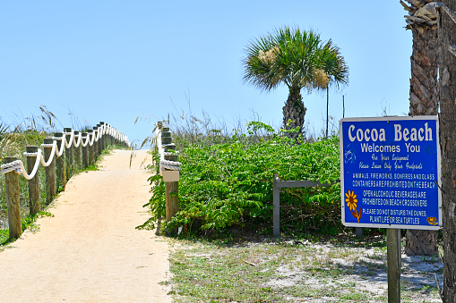 Sandy path over dunes with Cocoa Beach Welcomes You sign in Cocoa Beach, Florida.