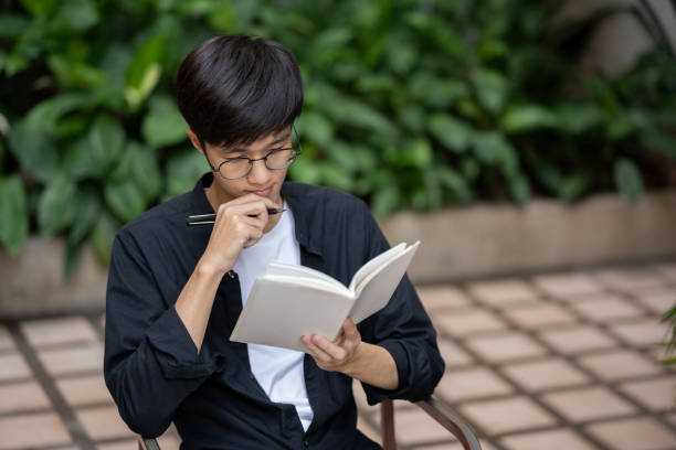 istock A focused Asian man is reading a book and working on his assignment at a table outdoors. 1938788836