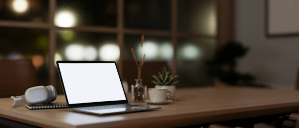 istock Modern office at night with a white-screen laptop computer and accessories on a table. 1938819464