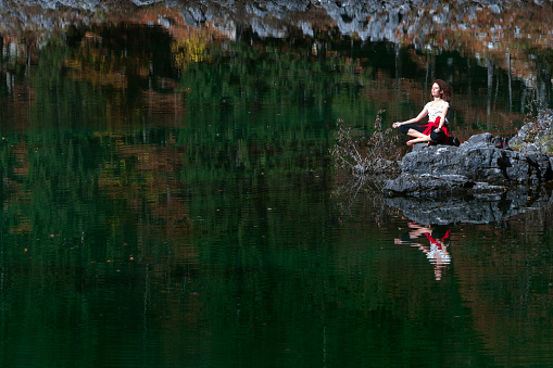 Caucasian Mid Adult Woman Meditation and relax on Coast of a Mountain Lake Tranquility Spot - Fusine Lakes, Tarvisio, Italy
