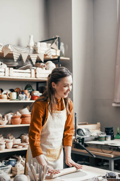 istock Smiling woman potter in her workshop, rolling out clay 1938972762