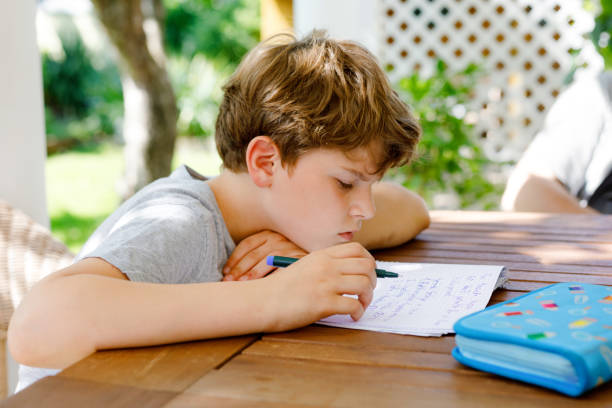 istock Hard-working sad school kid boy making homework during quarantine time from corona pandemic disease. Upset tired child on home schooling in coronavirus covid time, schools closed. Dad on background 1939004015