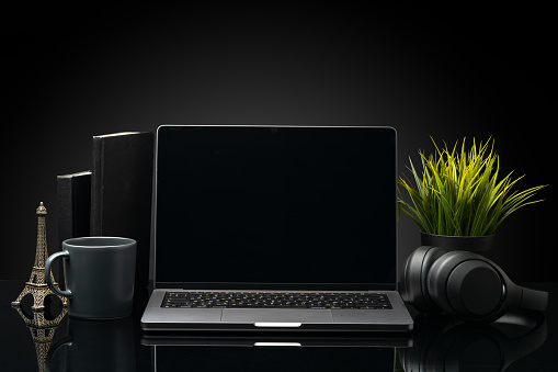 Laptop with black screen on working desk with cup and earphones on black background close up