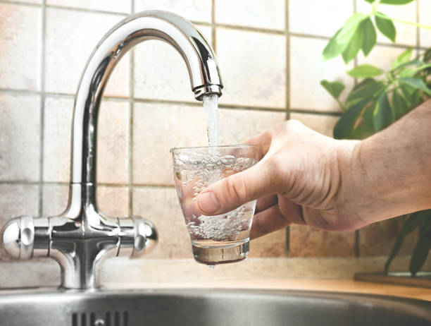 istock Man pouring water from faucet into glass in kitchen 1939019340