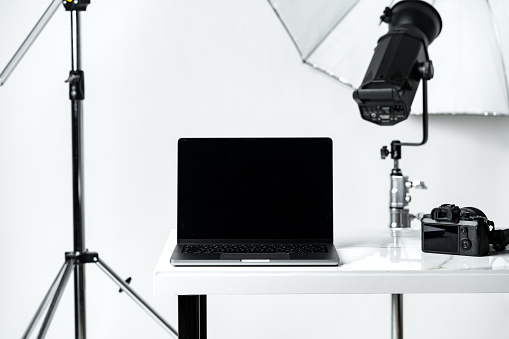 Laptop with black screen and photography equipment in photostudio close up