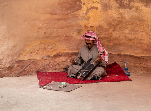 Wadi Musa, Jordan, October 05, 2023 : A Bedouin sits on the mat and plays the Bedouin one stringed lute for tourists in the Al Siq gorge in the Nabataean kingdom of Petra in the Wadi Musa city in Jordan