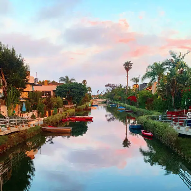 A quaint, colorful Venice canal framed by lush greenery complimented by a serene, illuminated cotton-candy sky.