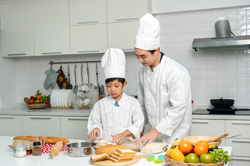 Young handsome asian man chef cooking breakfast in the kitchen. Happy asian man preparing food with ingredient. Chef in uniform in the kitchen.