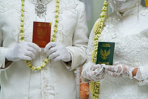 Bride and groom holding Indonesian marriage certificate. Marriage book or buku nikah as a legal sign of marriage in Indonesia. Wedding background, Selective focus