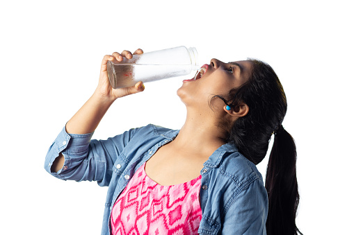 A pretty Indian young girl drinking cold water from glass bottle side facing in standing position