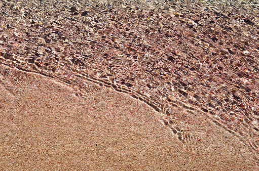 Sea surf on pink sand close up