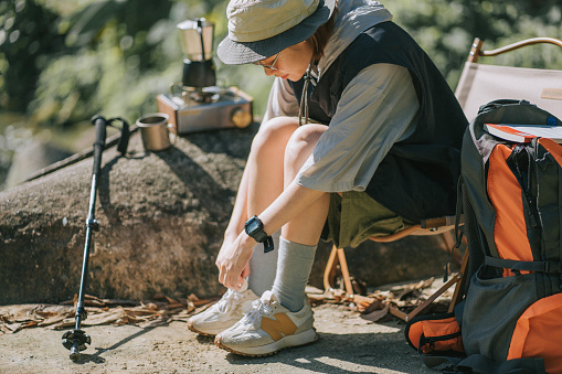 Asian Chinese young woman tying shoes lace outdoor nature beside river during weekend morning camping