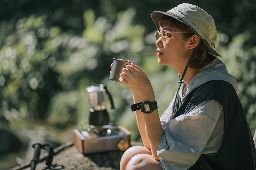 Asian Chinese young woman enjoying me time coffee outdoor nature beside river during weekend morning camping