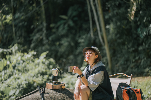 Asian Chinese young woman enjoying me time coffee outdoor nature beside river during weekend morning camping