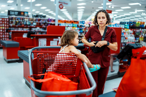 An Eurasian woman who is running errands after work with her three year old daughter, places her wallet back in her purse after paying for groceries at the checkout counter of a supermarket.