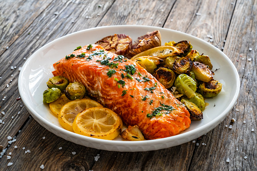 Fried salmon steak and garlic, brussels sprouts and lemon served on wooden table