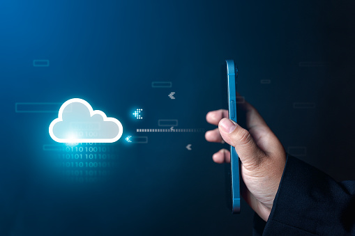 businessman's hand holds a smartphone with a virtual screen, linking data to the cloud on a large database, transferring data to a storage system via the internet - embracing cloud computing technology