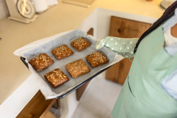 Portrait of happy woman in apron holding tray with fresh homemade bakery at modern kitchen.