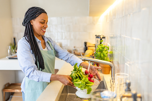 Photo of smiling woman washing fresh vegetables in the kitchen