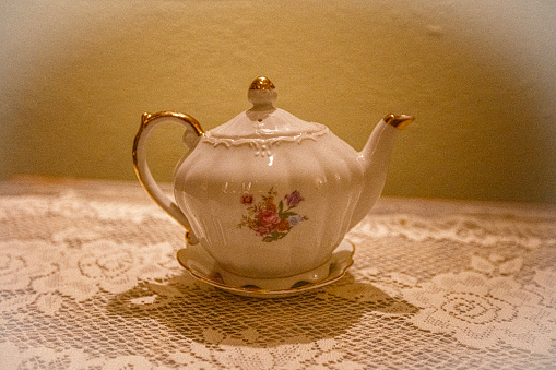 Antique tea pot with floral decoration on lace placemat.
