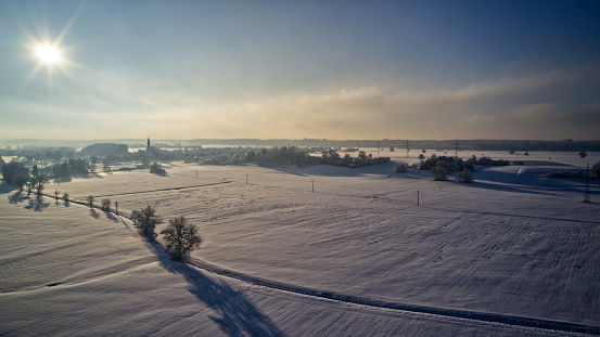 An aerial view of a winter landscape with a sunset casting a glow over a snow-covered field