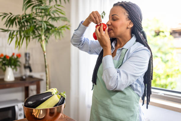 istock Afro woman smells a tomato in the kitchen 1939198644