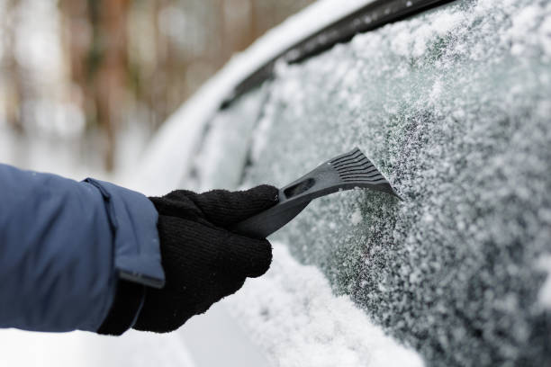 mężczyzna czyszczący oblodzoną szybę w samochodzie skrobaczką do lodu – zdjęcie