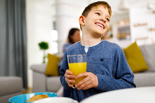 Happy boy enjoying while drinking fresh orange juice at home.